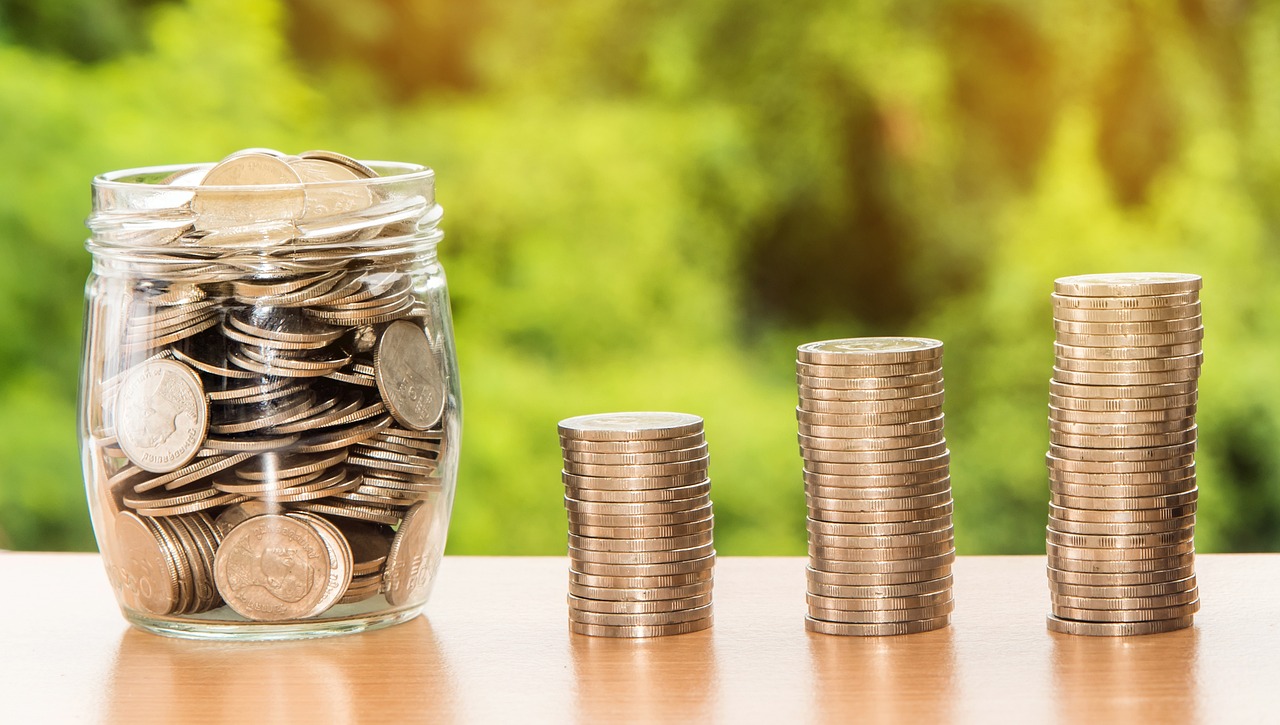 Money in a jar next to three piles of coins